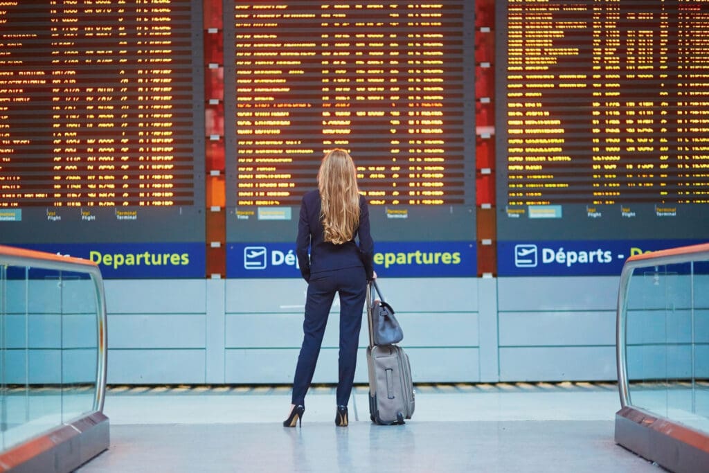 Traveler waiting at airport departure board showing how travel insurance can help with unexpected delays and disruptions