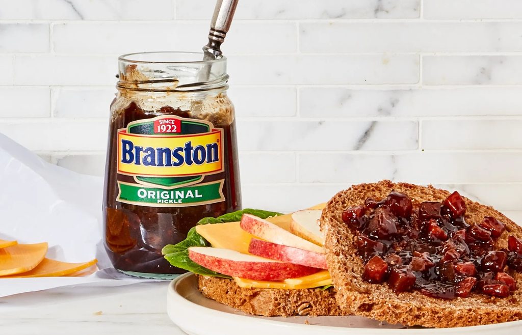 Jar of Branston pickle beside a cheese sandwich