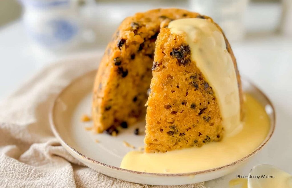 Sliced spotted dick pudding showing dried fruit, served with custard