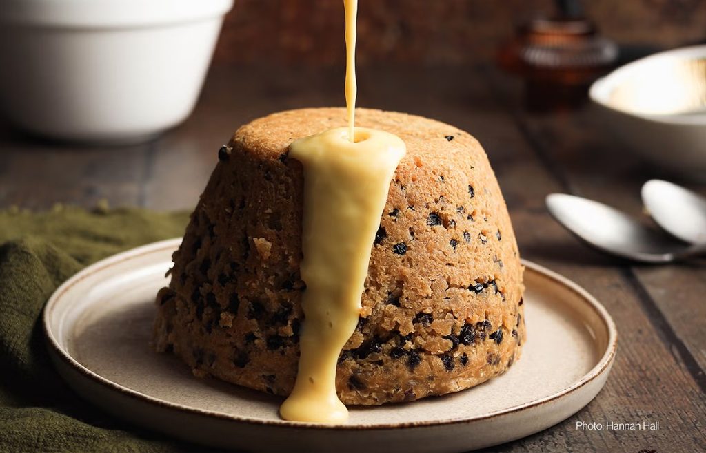Traditional spotted dick pudding with warm custard being poured over it